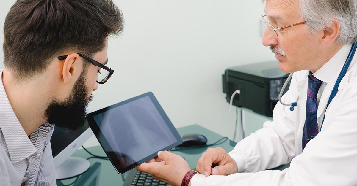 Mature Male Doctor Using A Digital Tablet For His Diagnosis.