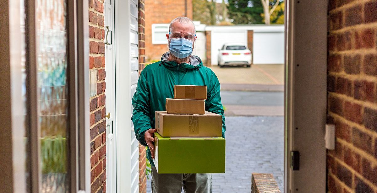 Home delivery man with parcels wearing face shield with mask
